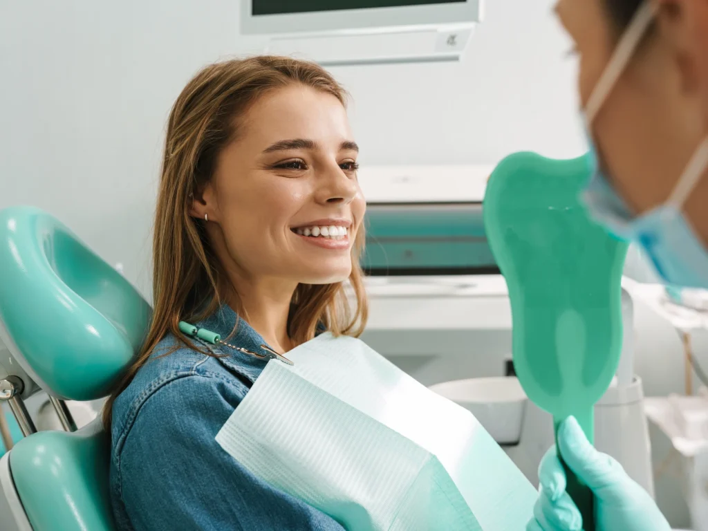 Young woman smiling in mirror after a teeth cleaning in Edmond, OK at Coffee Creek Family Dentistry